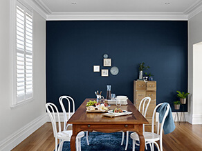 Dark navy blue feature wall white walls contrast with timber floor boards and table white chairs 